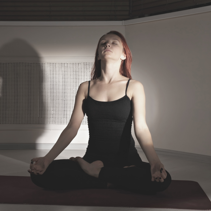 A woman practicing box breathing in her dimly lit room