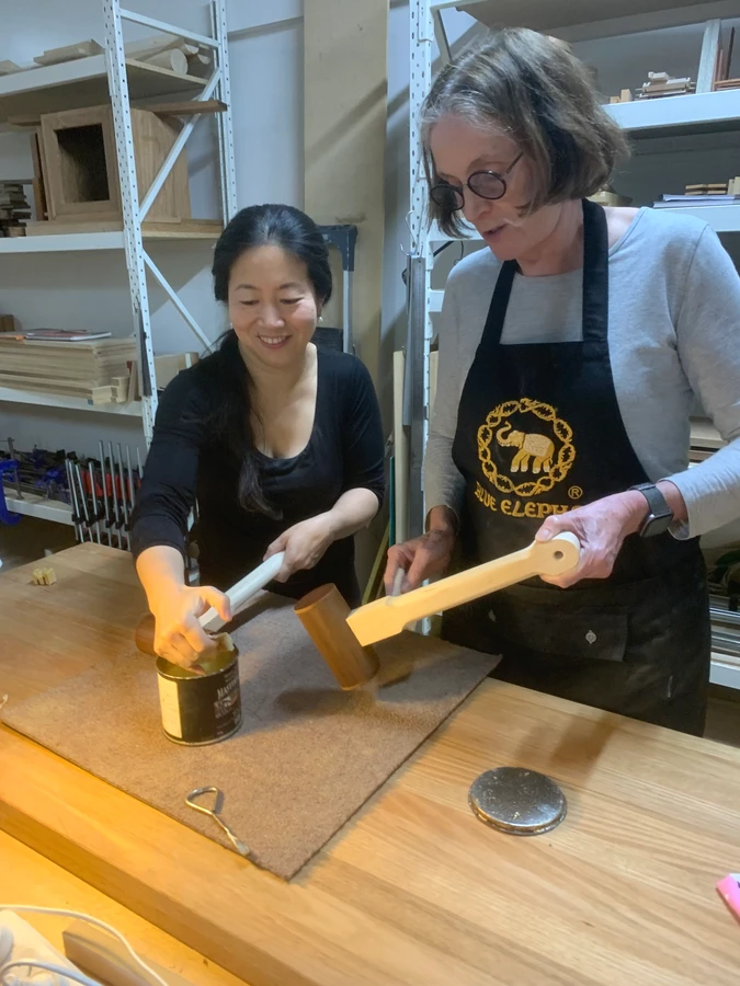 A teacher and student working on a wooden mallet at the bench.