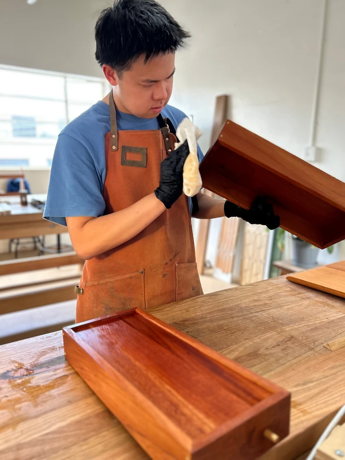 A student applying finish to the inside of a keepsake box lid.
