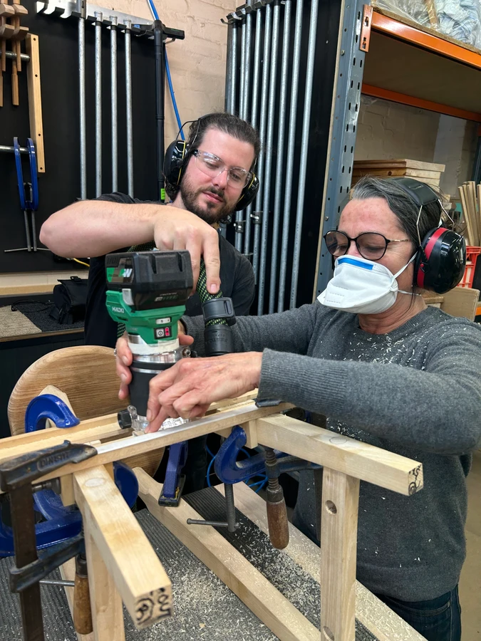 A teacher guiding a student using a router on a timber component.