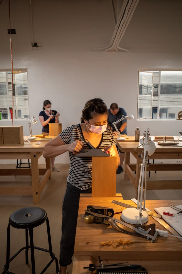 A student examining a timber board under a workshop lamp.
