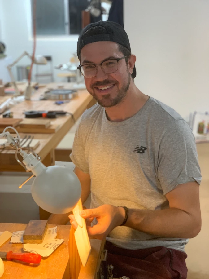 A student smiling while shaping a wooden knife at the bench.