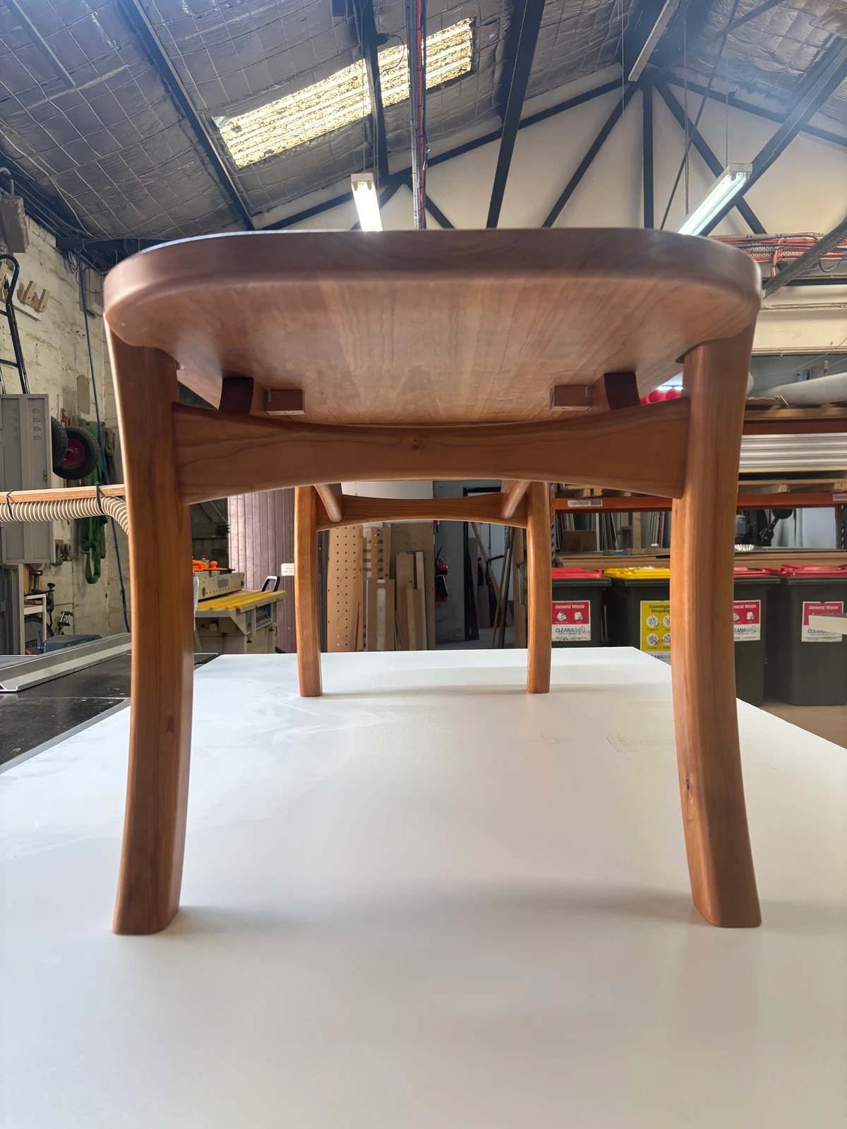 A timber stool with a shaped seat and legs on a workbench.