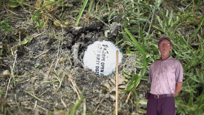 A person using the Range Ball Rescuer on a golf driving range, manually extracting deeply buried range balls from the ground