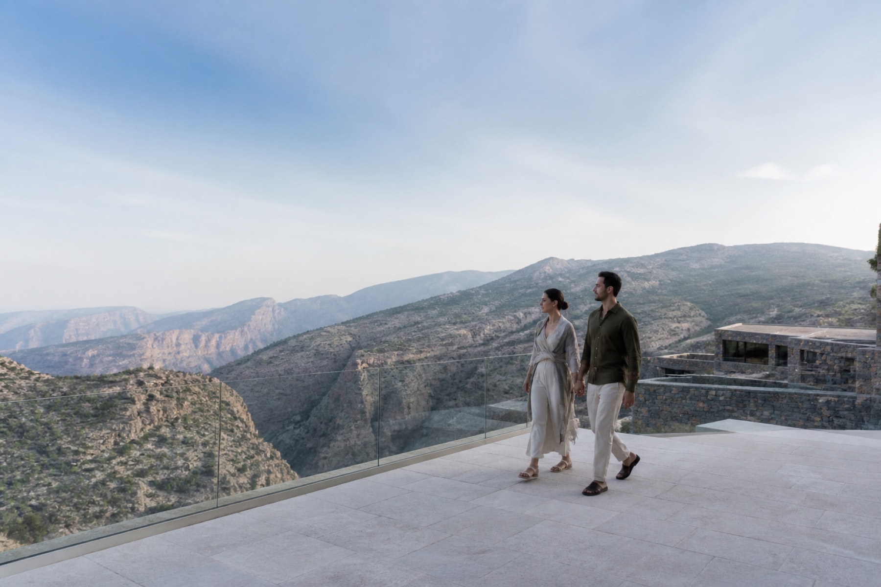 Cool morning view across Jabal Akhdar canyon with a couple walking on a restrained stone resort terrace; no décor.