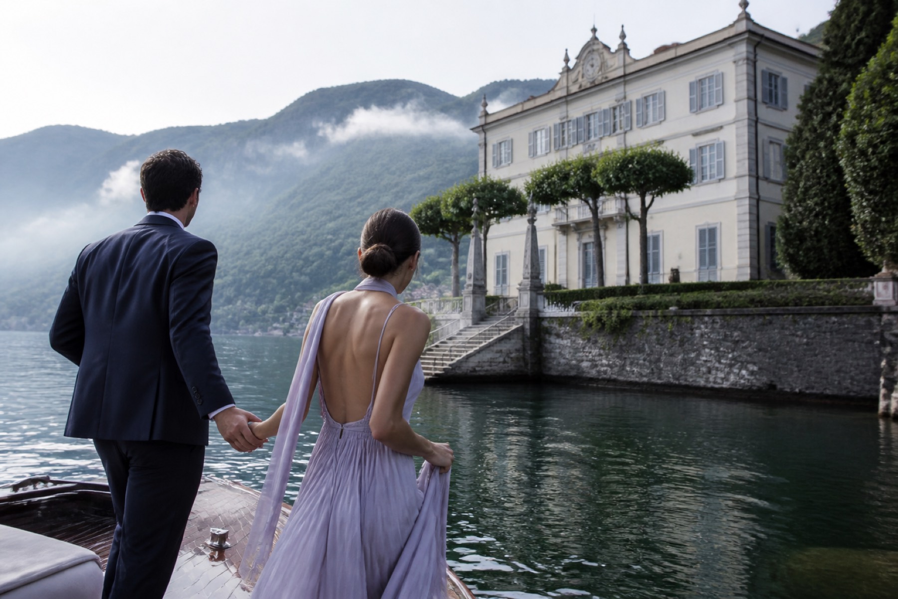 Cool bright Lake Como morning with a couple arriving by classic boat at a pale historic villa; no ceremony décor.