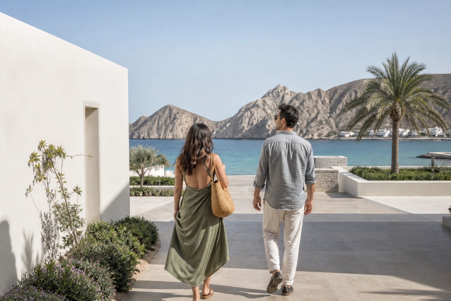 Airy Muscat seafront framed by mountains and white architecture with a couple entering a modern resort; no décor.