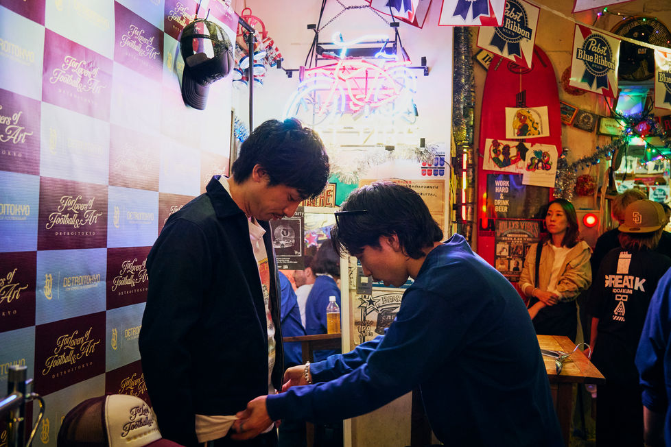 チェック柄の背景の前で談笑している2人の男性のスナップ写真。