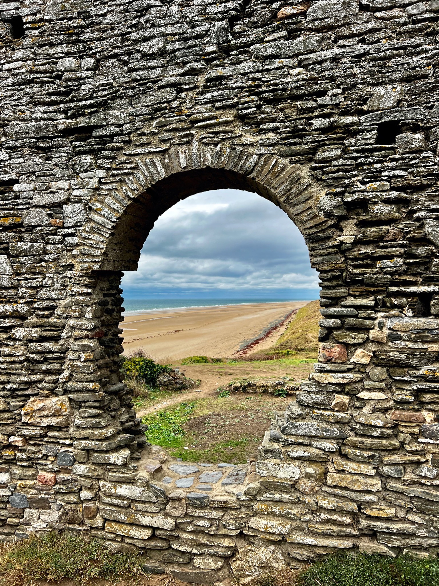 Sandy beach and sea framed by a historic stone arch on the North Wales coast