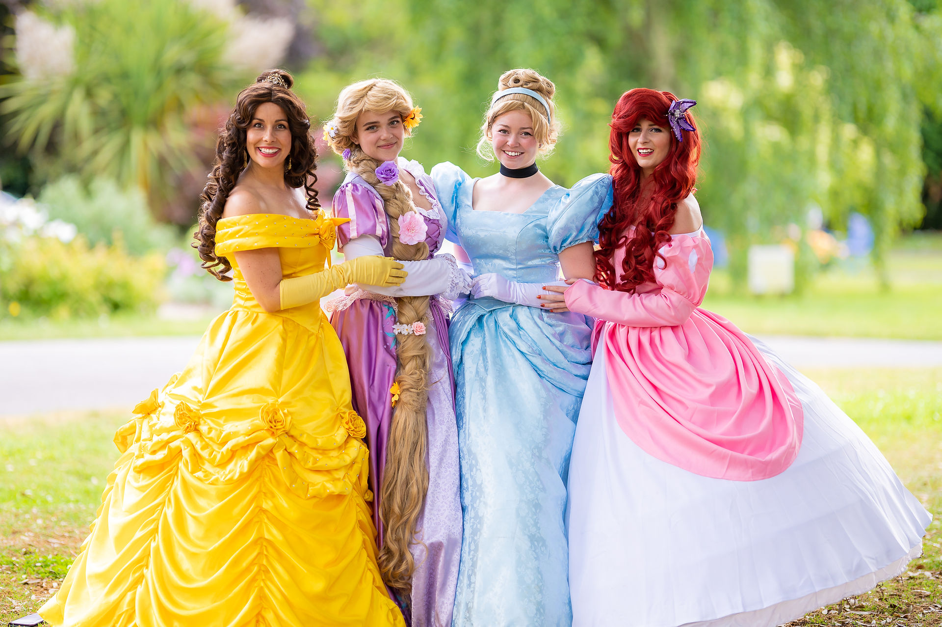 Belle, Rapunzel, Cinderella and Ariel stood together, holding hands, smiling at the camera