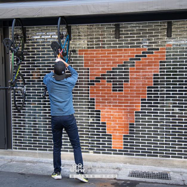 　　▊本案位於台北市一樓街角商業空間，牆面以「實心玻璃磚 × 紅磚搭配」構築出兼具現代感與地域特色的經典外牆。主要材質選用水波光紋理的實心玻璃磚，透過躺砌與交丁工法，兼顧透光與結構穩定性，使自然光可在日間自由穿透磚體，為空間帶入輕盈採光，展現沉穩而獨特的街角氣質。

最大亮點來自紅磚圖騰的設計巧思——這組紅磚排列正是業主品牌的 LOGO，藉由精密計算與模數整合，將品牌視覺語言融入建築外牆，不僅成為行人的視覺記憶點，也讓建築本身成為品牌精神的延伸與展示。此段設計展現了玻璃磚與紅磚搭配的高延展性，也是一種創意識別與材料整合的成功示範。

整體牆面結構更藏有穩固結構隱藏設計，讓牆體耐久安全，並整合黑色烤漆鐵件作為腳踏車掛架使用，兼顧實用性與外觀設計。此案充分體現森森專業施工團隊在現場整合、材料選用與光影設計的全面實力，是實心玻璃磚應用於商業空間的極佳案例。