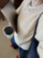 Woman in a cozy sweater holding a laptop and coffee, representing financial independence and flexibility.