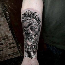 Skalletatuering med lågor och taggtråd, 'Human' text av Rowel Ink i Stockholm.	Dödskalletatuering med eld, taggtråd och texten 'Human' av Rowel Ink i Stockholm.
