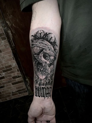 Realistisk underarmstatuering med dödskalle, törnekrona, lågor och gotisk text i svart och grått, utförd av tattoo studio stockholm.