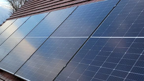 Solar panels on a red-tiled roof, angled under a blue sky. Bare trees in the background add contrast to the scene.