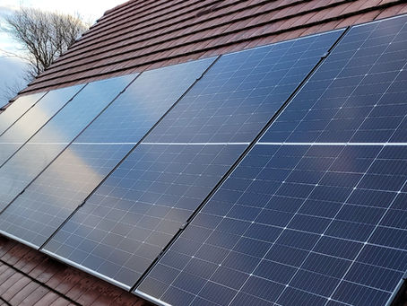 Solar panels on a red-tiled roof, angled under a blue sky. Bare trees in the background add contrast to the scene.