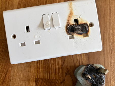 Burnt out moulded grey plug and burnt out white socket on wooden effect background