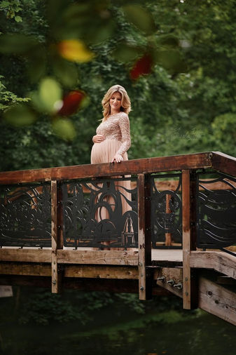 Donna incinta in abito pesca posa su ponte di legno in un parco durante servizio fotografico di gravidanza