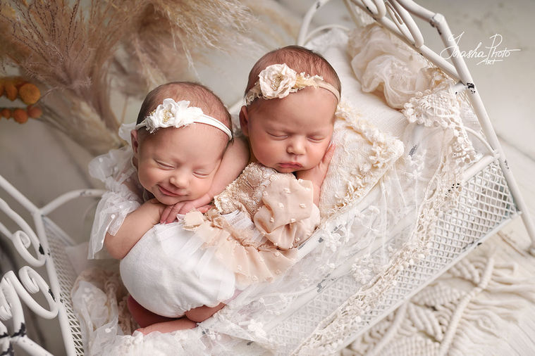 Newborn twins sleep cuddled in a white crib decorated with lace and flowers, artistic newborn photoshoot in romantic style