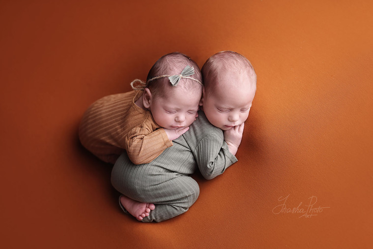 Newborn twins sleep hugging each other frontally on terracotta background, artistic newborn photoshoot with autumn palette