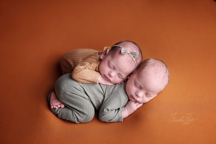 Newborn twins sleep hugging each other on terracotta background, artistic newborn photoshoot in autumnal shades