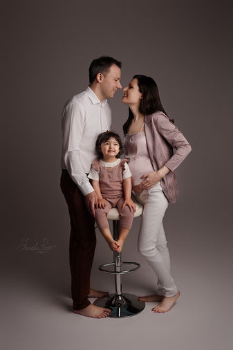 Smiling family with little girl sitting on stool between parents, pregnant mother caressing belly