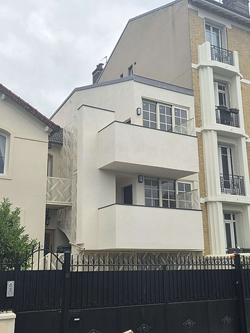 Bâtiment moderne blanc avec balcons derrière une clôture noire.