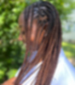 A black woman is shown from the side, smiling as she shows off her freshly braided hair in the outdoor area of The Sanctuary