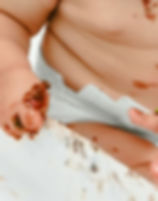 Baby's hand, stomach covered in messy fresh baby food delivery.