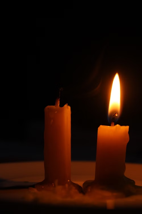 A photo of a dim candle with an unlit candle in a church.