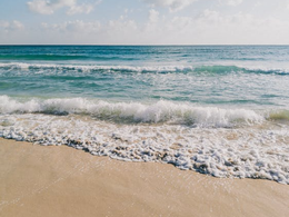 A photo of rolling waves at a beach with a bright sky.
