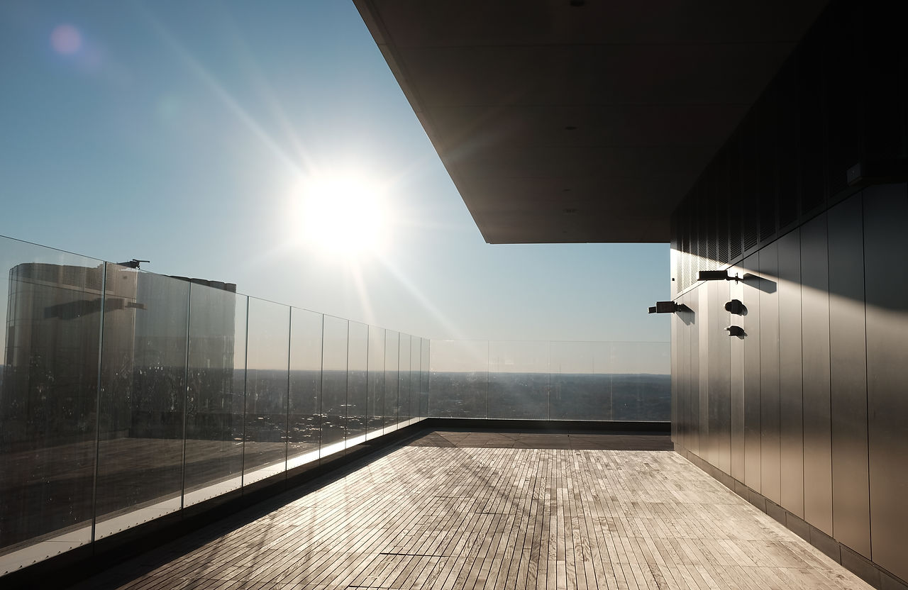 A sleek rooftop terrace bathed in sunlight, featuring a glass railing and modern architect