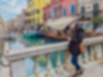 woman standing on a bridge in Venice and smiling while looking up at colorful buildings