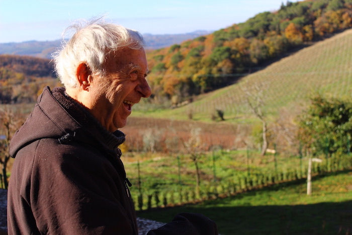 old man in a black hoodie laughing in front of a Fall landscape in Tuscany, Italy