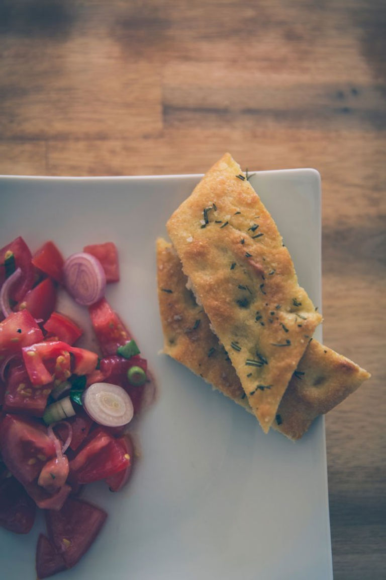 diagonal slices of italian herb focaccia on a plate next to tomato and onion bruschetta