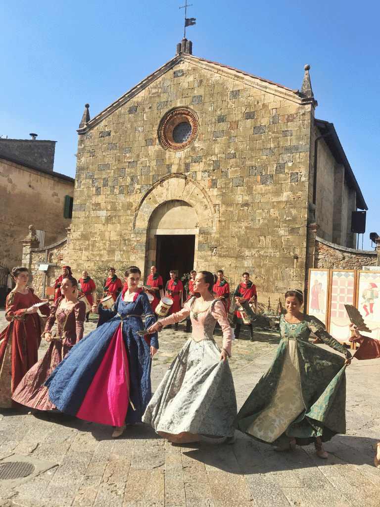 ladies dressed in fine medieval dresses with a line of drummers behind them
