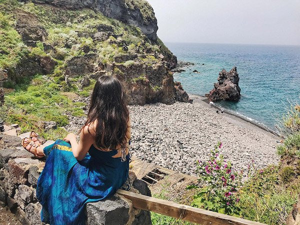 lady wearing a blue dress looking over a view of a rocky beach in the aeolian islands