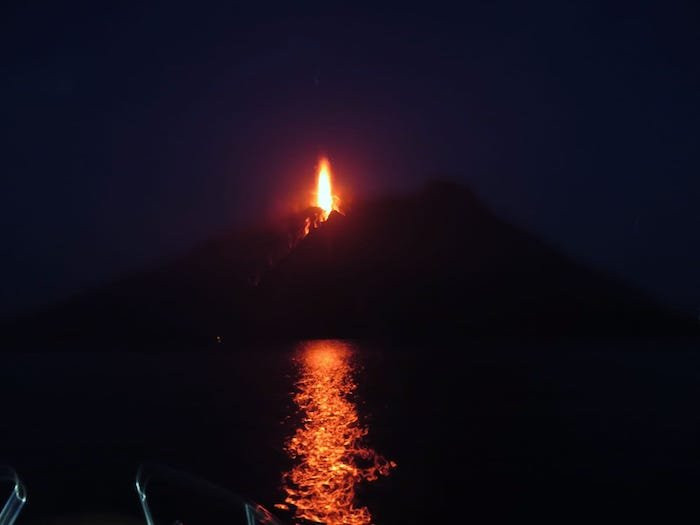 fire spewing from the volcanic island of Stromboli at night and the red reflection on the water