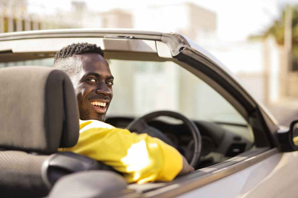 black guy in bright yellow shirt driving a convertible car
