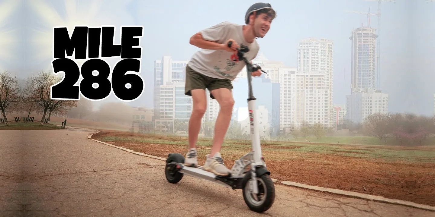 A person riding a Taur Scooter on a city street, surrounded by tall buildings and traffic.