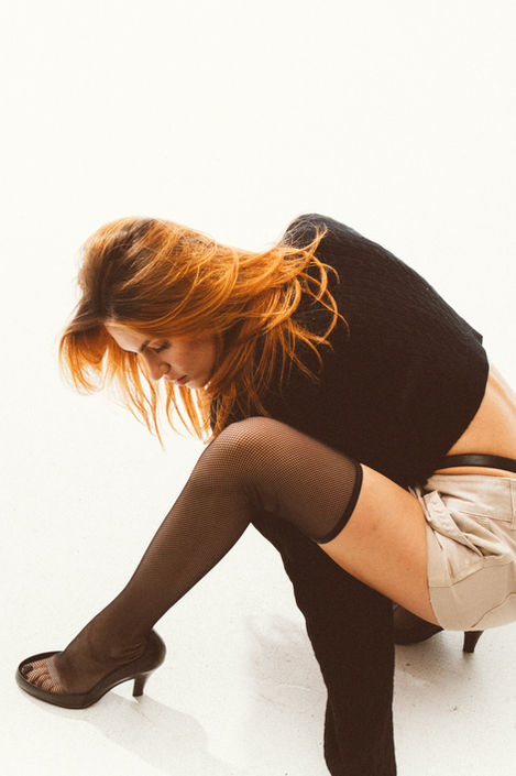 Seated fashion portrait with black sweater, tights, and minimalist studio backdrop