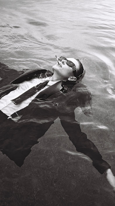 Black and white image of a model standing in water with a cinematic outdoor setting.