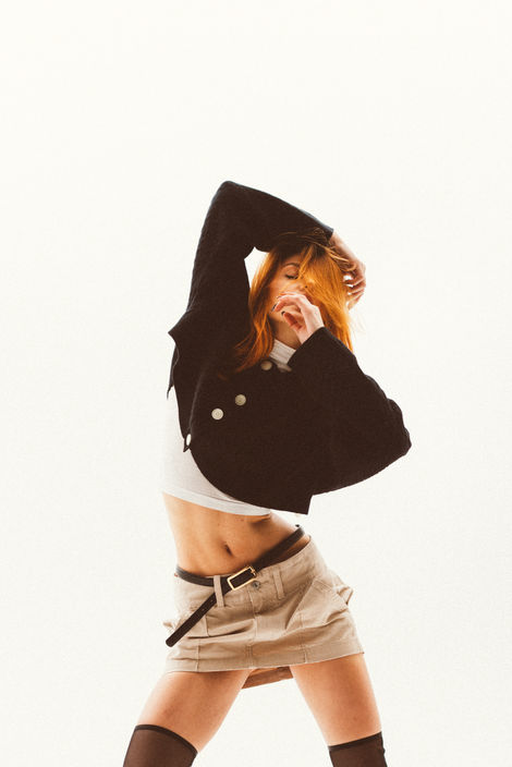 Fashion editorial portrait of model in black sweater and beige mini skirt photographed in studio