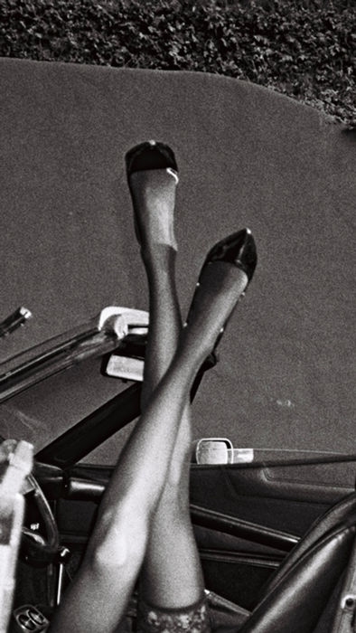 Black and white editorial image of model posing from a vintage vehicle