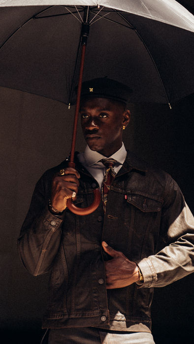 Cinematic fashion portrait of model beneath umbrella in tailored menswear