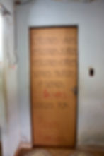 #paratodosverem: Porta marrom, na parte de dentro de uma casa, com uma frase escrita à mão: “Estamos vivos, estamos juntos, estamos fortes, somos muitos e somos loucos. Loucos por Bento Rodrigues”.