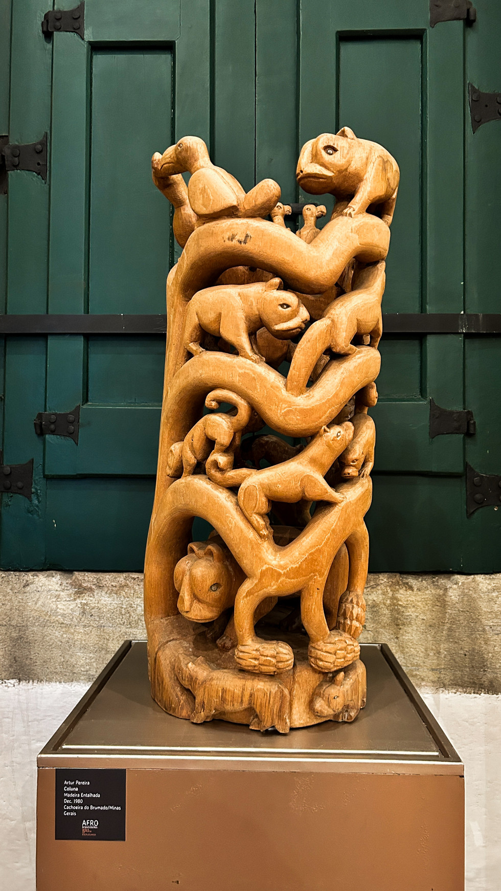 Na imagem, uma escultura em madeira traz representações de leões, macacos, antílopes e outros animais se entrelaçam em uma única peça.