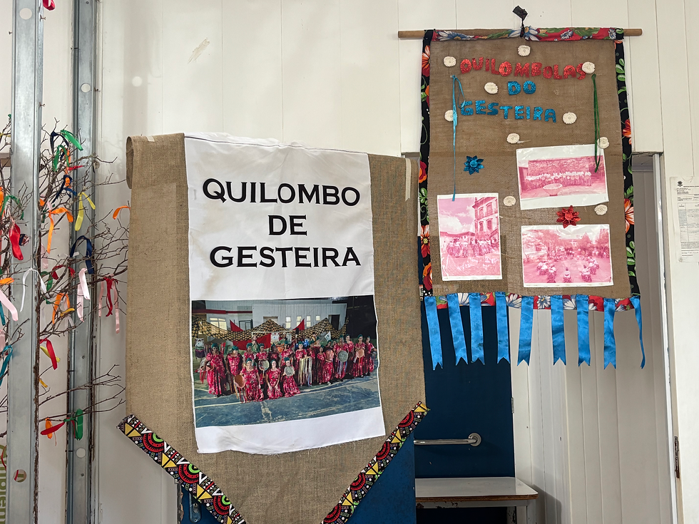 Homenagem ao grupo de dança Fênix localizado na Associação Quilombola de Gesteira. Foto: Lincol Moreira. #ParaTodosVerem: Painéis expositivos com a identificação do Quilombo de Gesteira e registros fotográficos da comunidade, fixados em um espaço interno decorado com elementos culturais.