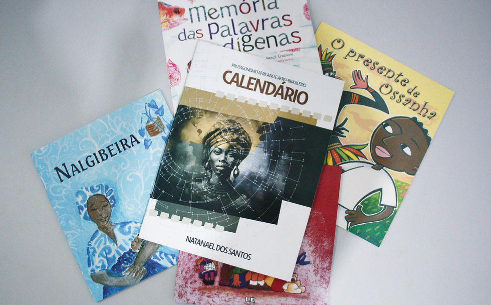 Com a obrigatoriedade do ensino de história e cultura afro-brasileira nas salas de aula, livros de literatura infantil com protagonistas pretos passam a fazer parte do cotidiano dos estudantes. Foto: Maria Clara Bispo. #ParaTodosVerem: quatro livros de literatura infantil com protagonistas negros, um calendário de protagonismos africano e afro-brasileira e uma bonequinha preta colocados sobre uma mesa.