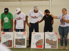 Para todos verem: Moradores atingidos e representantes de movimentos sociais protestam contra o projeto de longo prazo da Samarco em ato público. Com cartazes e falas críticas, denunciam os impactos previstos das novas pilhas de rejeitos em Bento Rodrigues, alertando para riscos socioambientais.